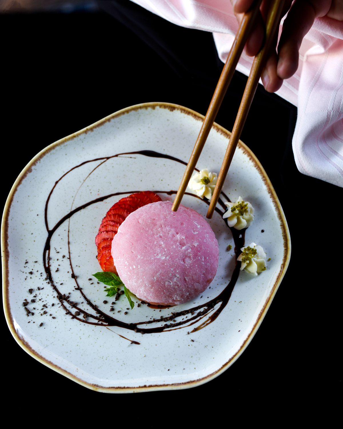 A pink mochi dessert on a speckled plate with strawberry and piped cream
